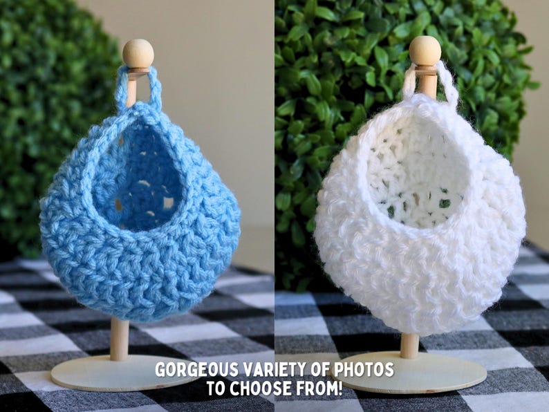 May include: Two crocheted hanging baskets, one blue and one white, are displayed on wooden stands. The baskets are made with a textured stitch and have a round shape.