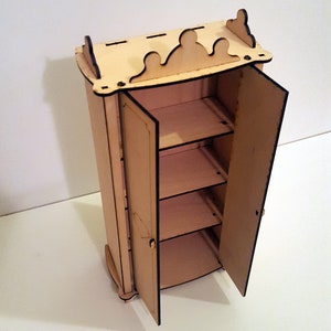May include: A wooden dollhouse-sized cabinet with two doors that open to reveal three shelves. The cabinet is made of light wood and has a decorative top.