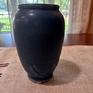 May include: A dark blue ceramic vase with a textured surface. The vase has a rounded body and a slightly flared rim. The base features a decorative swirl design. The vase is approximately 6 inches tall.