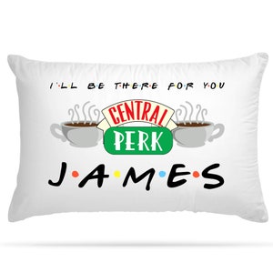 Puede incluir: Almohada blanca con un gráfico en blanco y negro del logotipo de Central Perk del programa de televisión Friends. El logotipo incluye dos tazas de café con vapor, las palabras "Central Perk" y el texto "I'll be there for you". Debajo del logotipo está el nombre "JAMES" en negro con puntos de colores entre las letras.
