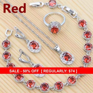 May include: A jewelry set featuring a silver-toned necklace, a bracelet, a ring, and a pair of drop earrings. Each piece is adorned with oval-shaped red gemstones surrounded by small clear stones. The word Red is printed in the top left corner.