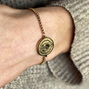 May include: A gold chain bracelet with a round pendant featuring a religious image and the text "EIVS IN OBITV-NRO-FR-A" and "HAEC SIGNA-VINC-E".