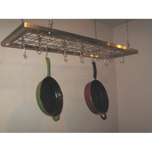 May include: A stainless steel pot rack with hooks hanging from the ceiling. Two pots are hanging from the hooks, one is green and one is red.