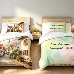May include: Two twin beds with white wooden frames and headboards. The left bed features a duvet and pillowcase with a printed European village street scene. The right bed features a duvet and pillowcase with a pastel watercolor design and the text Your Custom Image/Text.