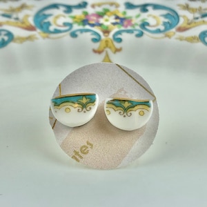 May include: A pair of white ceramic earrings with a blue and gold design. The earrings are shaped like half circles and have a delicate floral pattern.