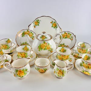 May include: A complete vintage tea set with a teapot, cups, saucers, milk jug, sugar bowl and serving plate. The white porcelain is decorated with yellow roses and gold edging. A classic tea service for afternoon tea.