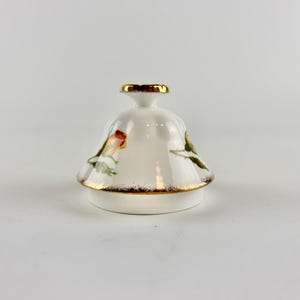 May include: A white ceramic lid with a gold rim and detailing. The lid has a floral design with red, yellow, and green accents. Likely for a teapot or sugar bowl.
