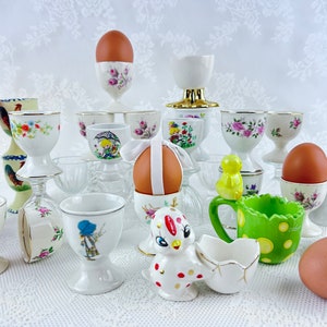 May include: A collection of various egg cups, some with floral designs, others with animal motifs, and some with plain white designs. There are also several brown eggs in the egg cups.