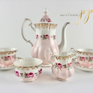 May include: A pink and white tea set with gold accents and floral designs. The set includes a teapot, creamer, sugar bowl, and two teacups and saucers.