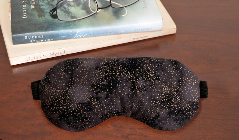 K&ouml;nnte beinhalten: Eine schwarze Schlafmaske mit goldenen Glitzer. Die Maske ist aus weichem, pl&uuml;schem Stoff und hat ein elastisches Band.
