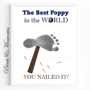 May include: Framed print with the text "The Best Poppy in the WORLD" and "YOU NAILED IT". It features a grey footprint, a brown hammer, and small nails. The print has the words "Prints & Memories" in the corners.