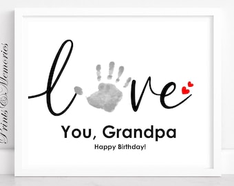 May include: A white framed print with the word "love" in black cursive lettering. A gray handprint is incorporated into the word "love". The text "You, Grandpa Happy Birthday!" is printed below the word "love".