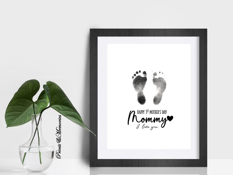 Pu&ograve; includere: Una stampa d'arte stampabile in bianco e nero con un design ad acquerello di due impronte di piedi di bambino. Il testo recita "Happy 1st Mother's Day! Mommy I love you" con un cuore.