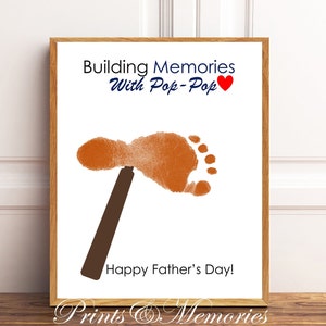 May include: A framed print with a brown wooden frame. The print features a brown footprint with a brown hammer, the text "Building Memories With Pop-Pop" and "Happy Father's Day!" on a white background.