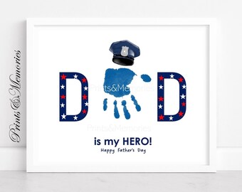 Puede incluir: Una impresión enmarcada con la palabra "DAD" en azul con estrellas rojas y blancas. Una huella de mano azul y un sombrero de policía están en el centro. El texto "is my HERO! Happy Father's Day" está debajo. La impresión está en un marco blanco.