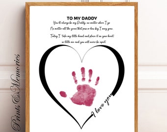 May include: A framed print with a wooden frame. The print features a black heart outline with a pink handprint inside. Text reads "To My Daddy" and a loving message. The words "I love you" are written on the heart.