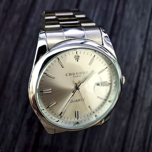 May include: A silver wristwatch with a white face and black hands. The watch face has the words "Chronos Time Quartz" printed on it.