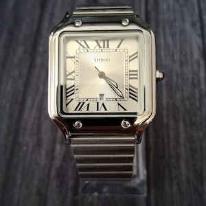 Puede incluir: Reloj de pulsera plateado con esfera cuadrada y correa metálica. La esfera es blanca con números romanos negros y la marca "YHMEI". La fecha se muestra en la parte inferior. El reloj tiene una correa metálica plateada.