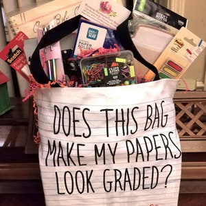 May include: A white tote bag with the text "Does this bag make my papers look graded?" and "Mrs. Funnell Woodland Elementary" printed on it. The bag is filled with school supplies, including folders, paper clips, sticky notes, and pens.