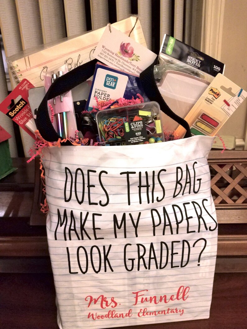 May include: A white tote bag with the text "Does this bag make my papers look graded?" and "Mrs. Funnell Woodland Elementary" printed on it. The bag is filled with school supplies, including folders, paper clips, sticky notes, and pens.