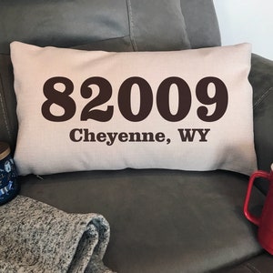 May include: A beige throw pillow with the text "82009 Cheyenne, WY" printed in black.