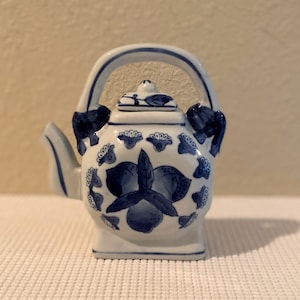 Op de afbeelding: Een klein blauw en wit porseleinen theepot met een bloemenmotief. De theepot heeft een handvat en een tuit.