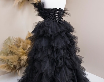 Op de afbeelding: Een zwarte strapless tule jurk met een gelaagde rok en een satijnen lijfje. Het lijfje heeft een veter aan de achterkant.