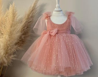 Puede incluir: Un vestido de tul rosa con un corpiño blanco y un lazo rosa. El vestido tiene un estampado de lunares y es perfecto para una ocasión especial.