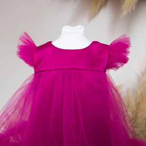 Peut inclure: Une robe en tulle magenta avec un corsage en satin et des manches bouffantes. La robe est sur un mannequin blanc.