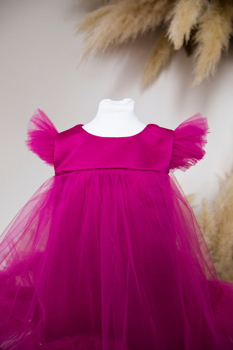 Peut inclure: Une robe en tulle magenta avec un corsage en satin et des manches bouffantes. La robe est sur un mannequin blanc.