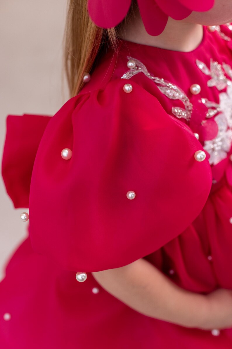 Puede incluir: Un vestido rosa brillante con mangas abullonadas y adornos de perlas. El vestido tiene un dise&ntilde;o de encaje blanco en el corpi&ntilde;o.