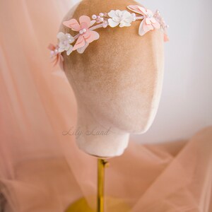 May include: A delicate floral crown with pink and white flowers, accented with pearls and beads. The crown is displayed on a mannequin head.
