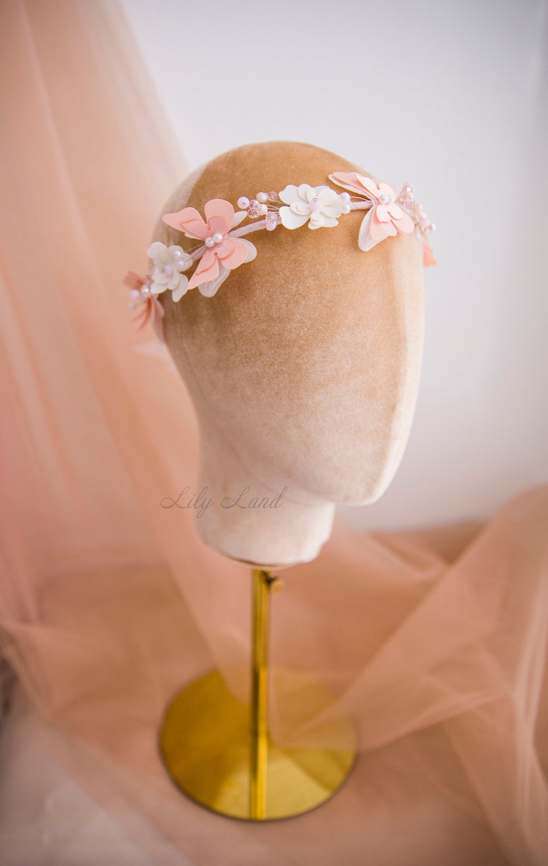 May include: A delicate floral crown with pink and white flowers, accented with pearls and beads. The crown is displayed on a mannequin head.