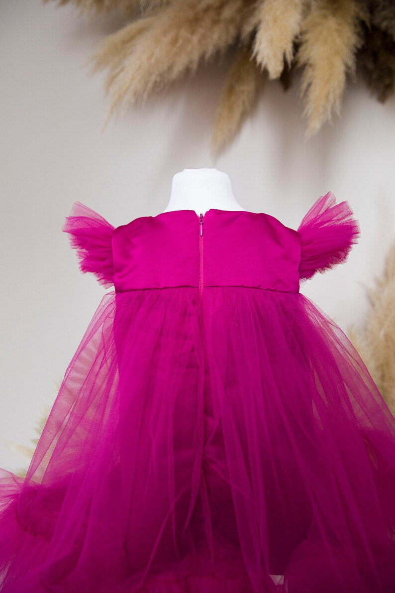 Peut inclure: Une robe en tulle magenta avec un corsage en satin et des manches bouffantes. La robe a une fermeture &eacute;clair dans le dos.
