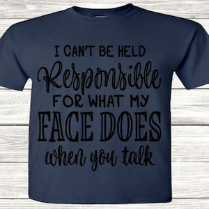 Könnte beinhalten: Ein marineblaues T-Shirt mit dem Text "Ich kann nicht für das verantwortlich gemacht werden, was mein Gesicht tut, wenn du sprichst" in Schwarz gedruckt.