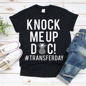 Puede incluir: Camiseta negra con texto blanco que dice "Knock Me Up Doc! #Transferday" y un gráfico de piña.