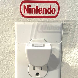 May include: A white night light plugged into a standard electrical outlet. The night light has a clear plastic cover with the word "Nintendo" printed in red.