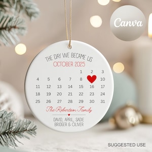 May include: A round white ceramic ornament with a gold string, displaying a calendar for October 2025. The text reads "The Day We Became Us" and "The Robertson Family." A red heart marks the 16th. Names are listed below the calendar.