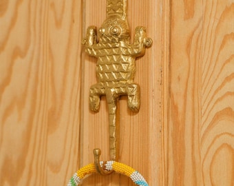 Peut inclure: Un crochet en forme de lézard doré monté sur une porte en bois. Un collier de perles coloré est suspendu au crochet.