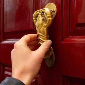 Hand opening a red door with a decorative gold lobster door knocker