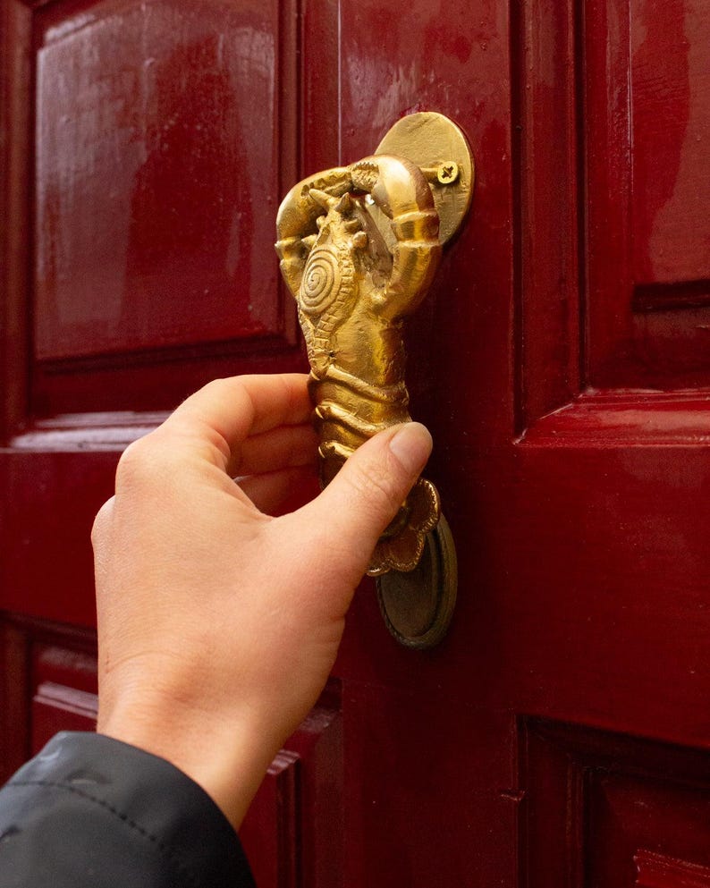 Hand opening a red door with a decorative gold lobster door knocker
