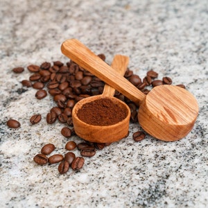 Könnte beinhalten: Zwei Holzlöffel, einer mit gemahlenem Kaffee gefüllt, umgeben von Kaffeebohnen auf einer gesprenkelten grauen Oberfläche.