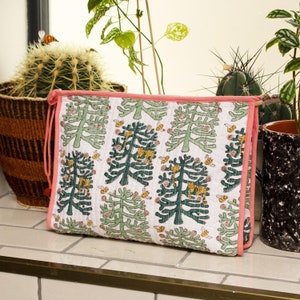 Può includere: Una trousse da trucco trapuntata in cotone bianco con un bordo rosa. La trousse presenta un motivo ripetuto di alberi verdi con api gialle e tigri arancioni.