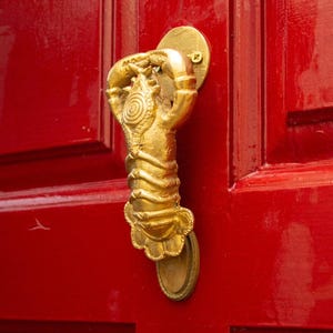 Gold door handle shaped like a lobster on a red door