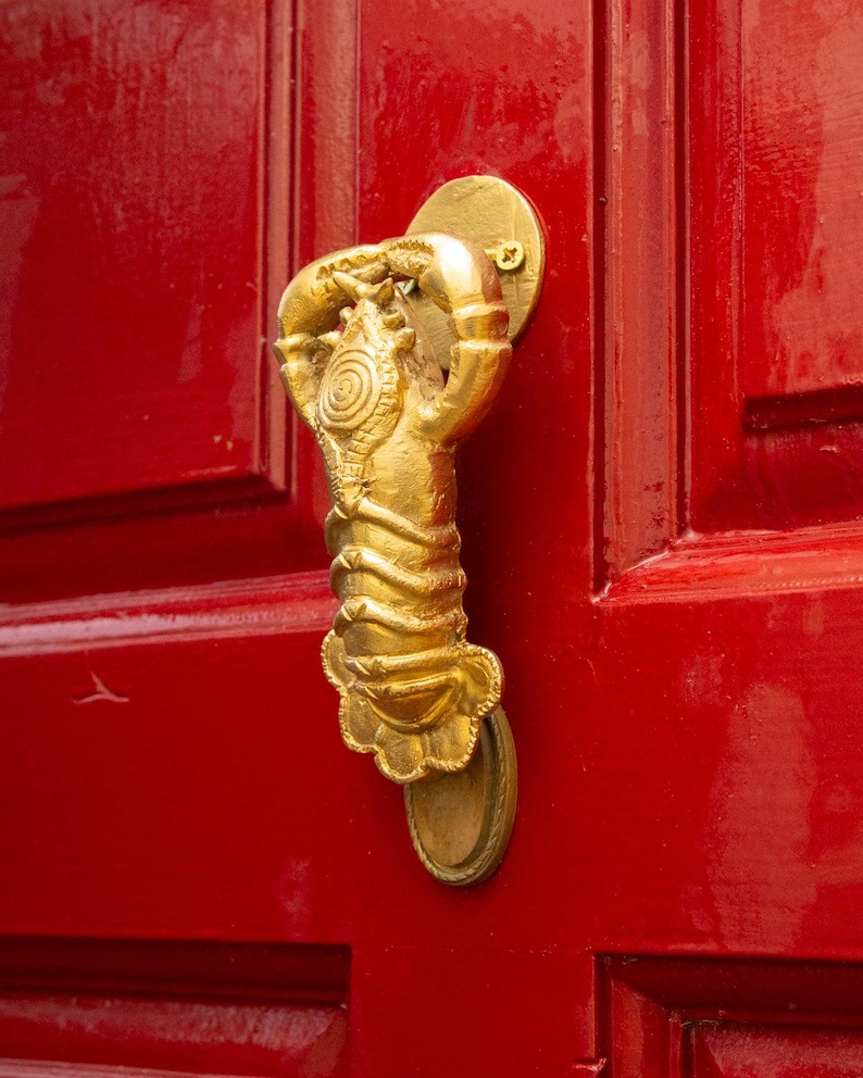 Gold door handle shaped like a lobster on a red door