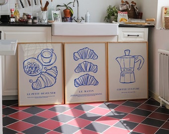 May include: Three framed prints with blue illustrations on a white background. The prints are hung on a white wall above a white kitchen sink. The prints feature a croissant, a coffee pot, and a croissant with a bowl of berries. The text on the prints reads "Le Petit Dejeuner", "Le Matin", and "Coffee Culture".