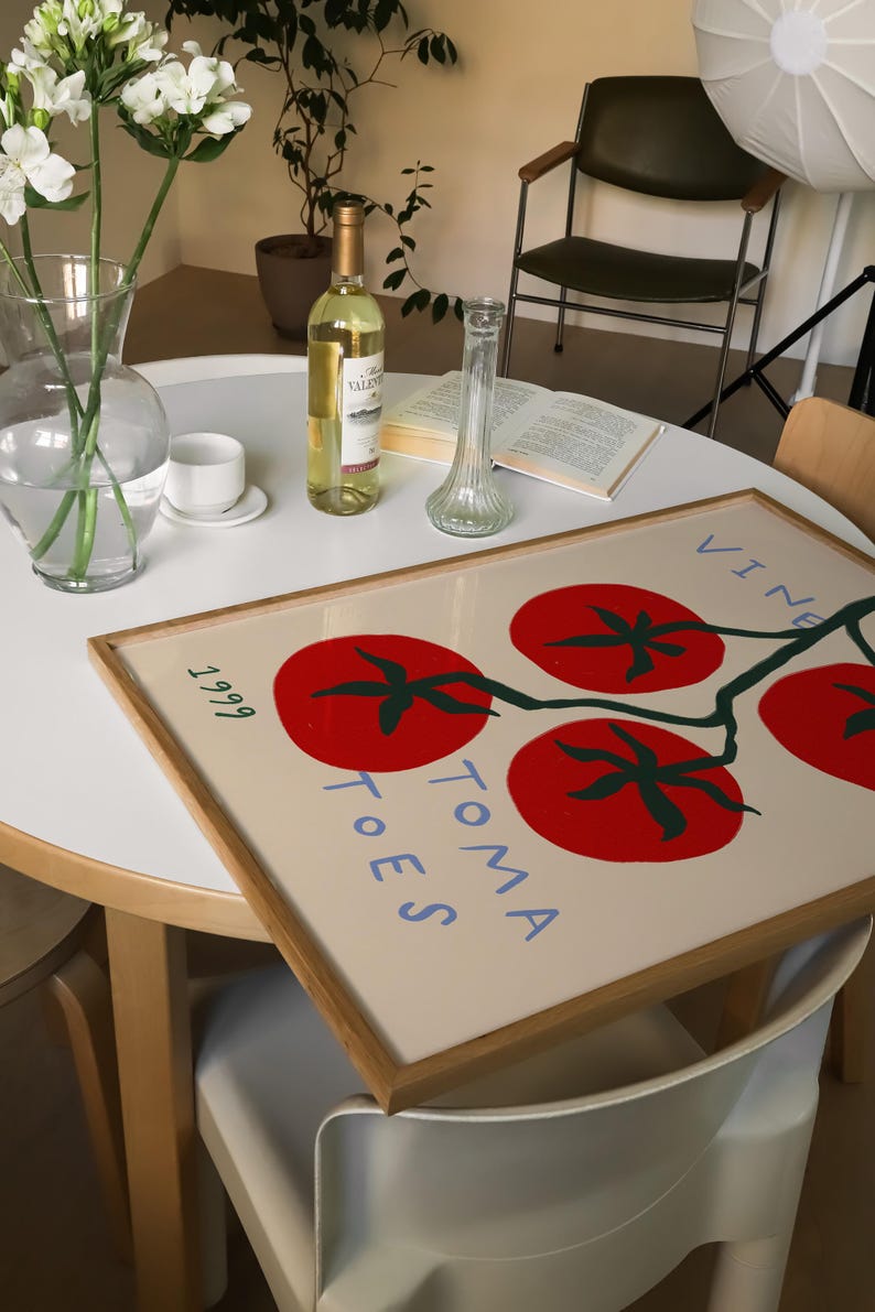 May include: A framed print with a white background and a stylised illustration of red tomatoes on a vine. The text "TOMA TOES" is written in blue on the print. The print is framed in a natural wood frame.