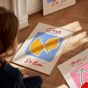 May include: A framed print with a blue background and two yellow lemons. The text "C'est Paris" is written in red and blue, and "Si Bon" is written in red. The year "1999" is written in black.