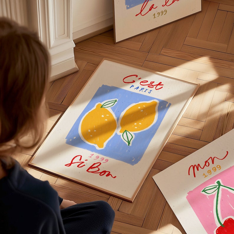 May include: A framed print with a blue background and two yellow lemons. The text "C'est Paris" is written in red and blue, and "Si Bon" is written in red. The year "1999" is written in black.