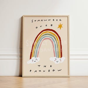 Op de afbeelding: Een ingelijste kunstprint met een kleurrijke regenboog en de tekst "Somewhere Over The Rainbow". De regenboog bestaat uit rode, oranje, gele, groene, blauwe en roze bogen. Twee lachende wolken staan aan de basis. Een gele ster staat erboven.